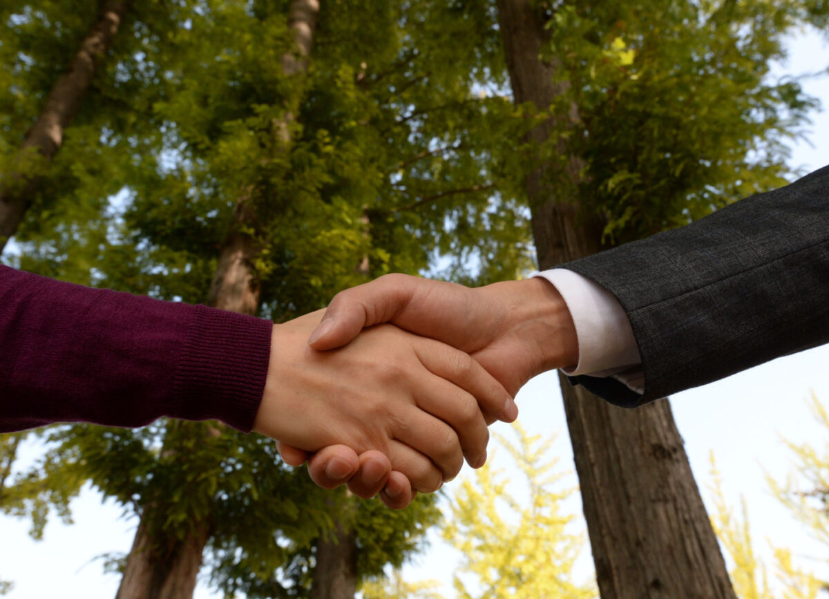 Sustainability partners enrich Domtar's sustainability journey. Photo of handshake with backdrop of trees.